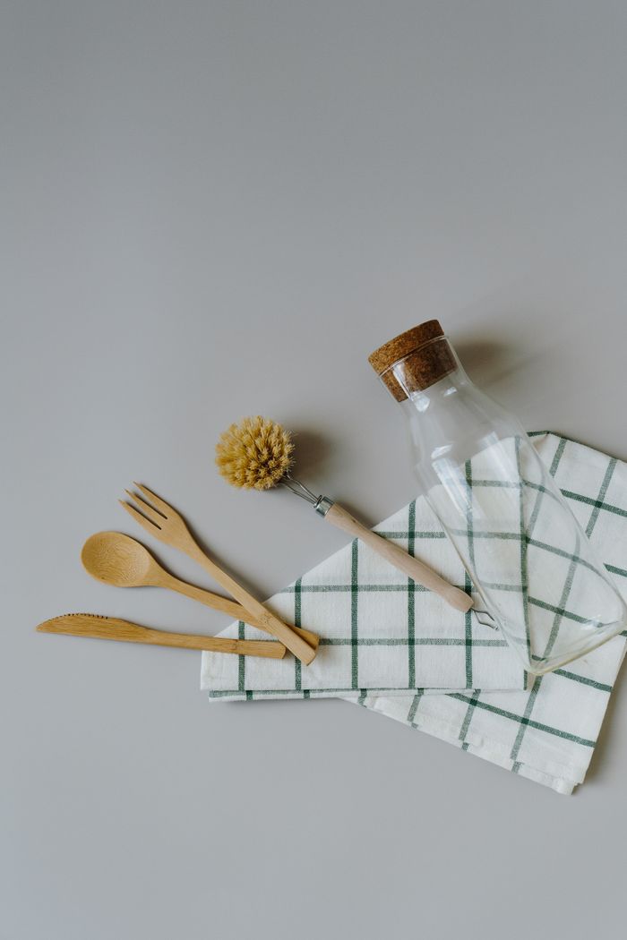 A flat lay of eco-friendly kitchen utensils including a glass bottle on a cloth.